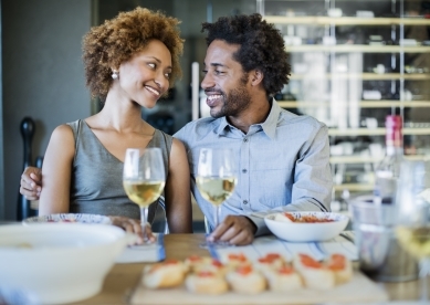 Couple sitting in restaurant holding wine glass with white wine and looking at each other while smiling.